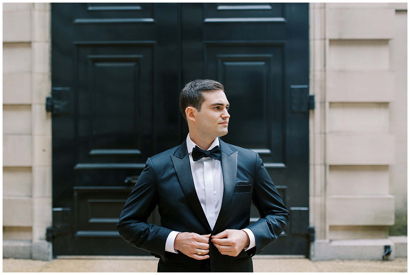 Groom in black tux buttoning jacket in front of the entrance of the Larz Anderson House 