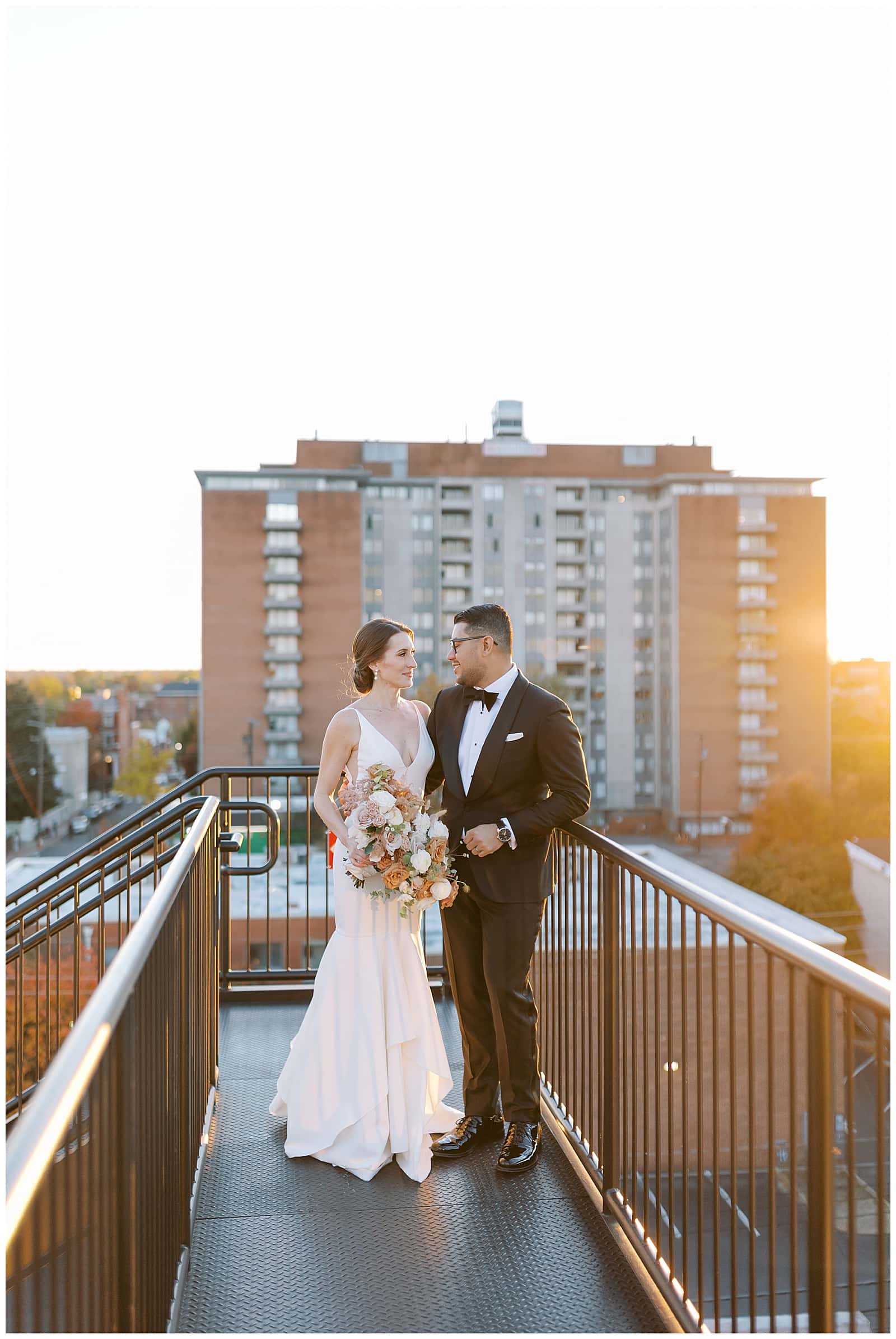 Sunset photo of a bride and groom on the rooftop of Common House Richmond embracing in a wedding dress and black tux