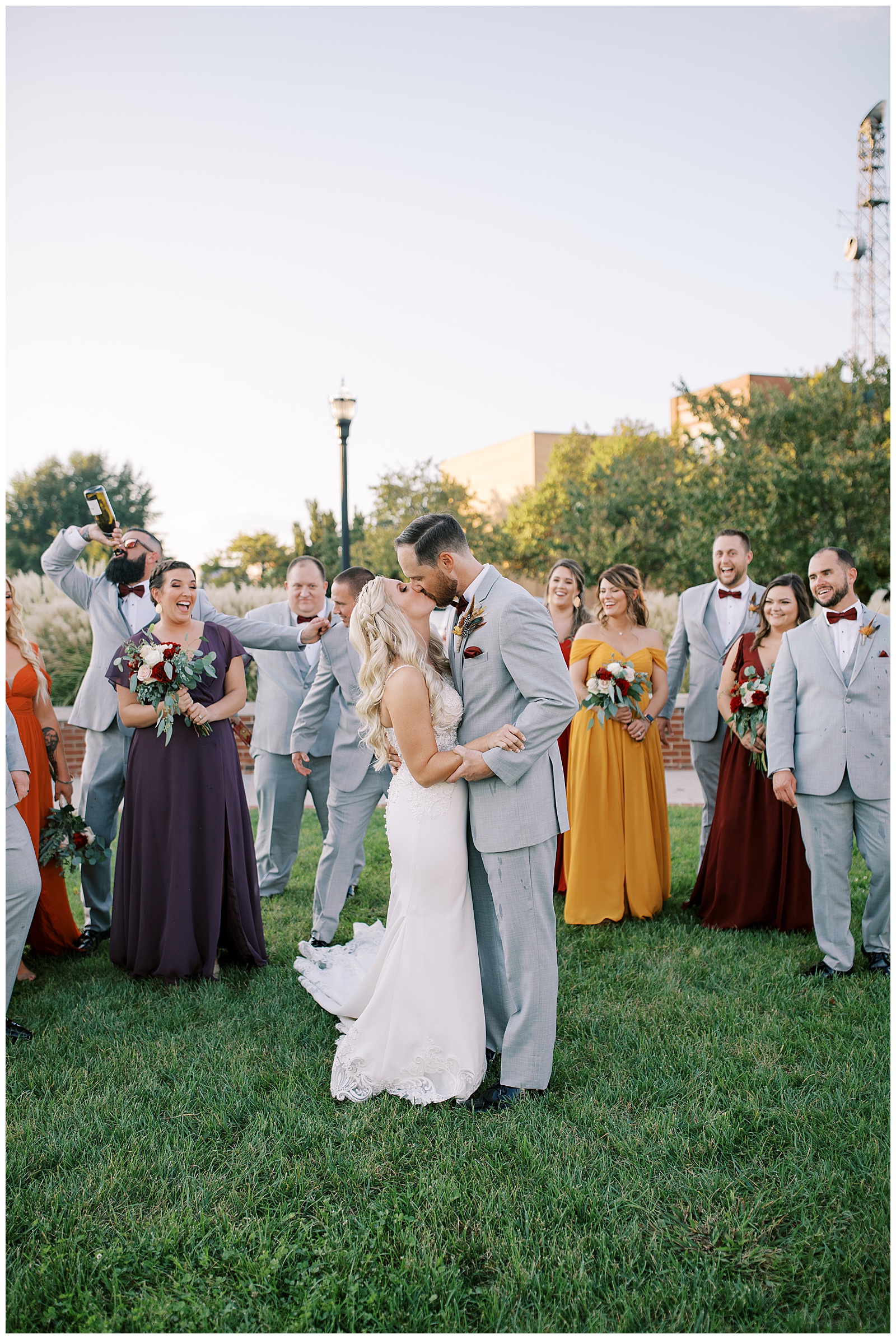 A bride and groom in wedding attire stand in front of a group of wedding party whilst they cheer them on and kiss in front of The Social venue in Kingsport Tennessee