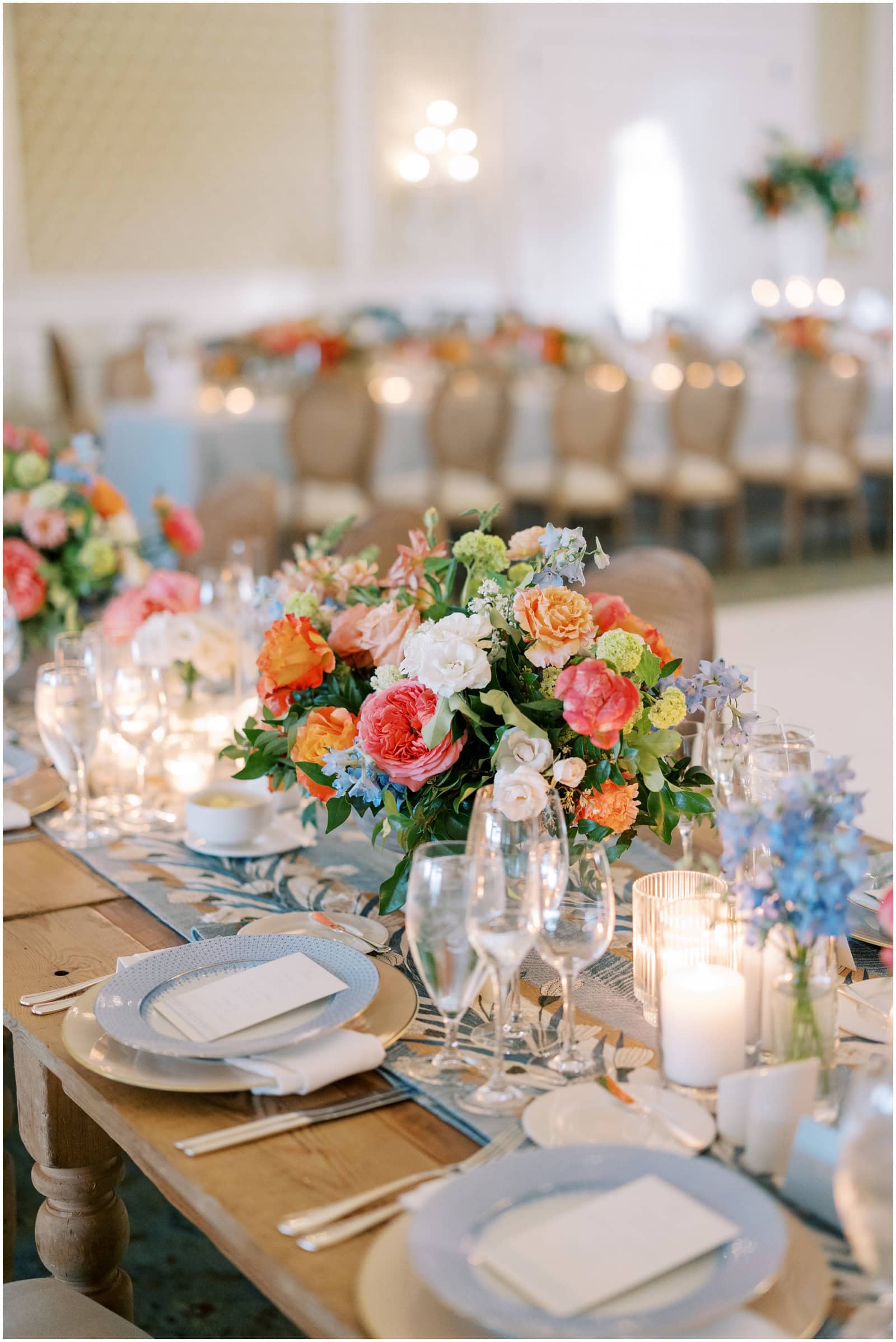 Vibrant floral centerpiece on a wedding reception table with elegant place settings and candlelight ambiance.